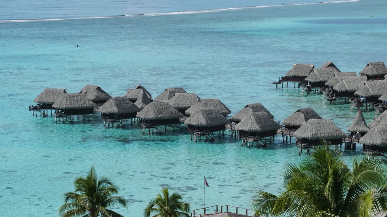 Detail of overwater bungalows, palm trees, white sand beaches and a coral reef on a sunny day in Moorea, French Polynesia.