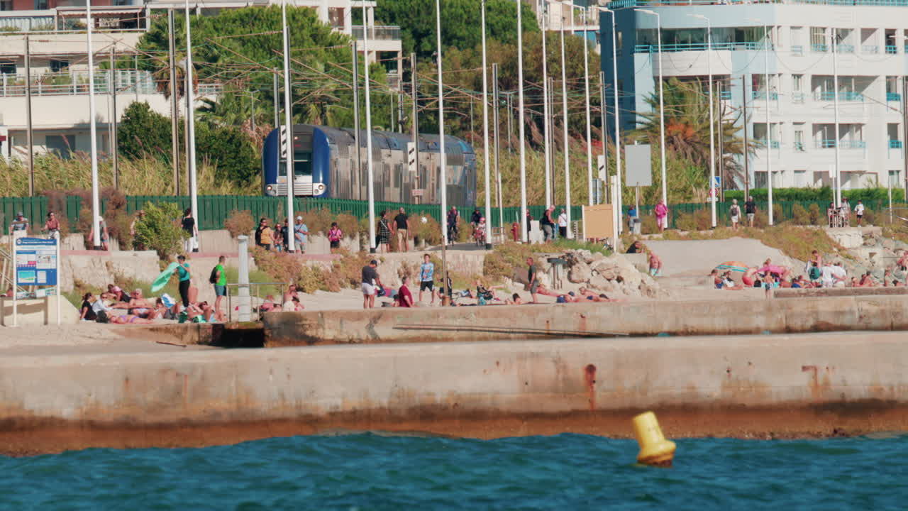 Cannes, France - October 6, 2025: A modern train passes along the coastline near the beach, while people walk and relax nearby