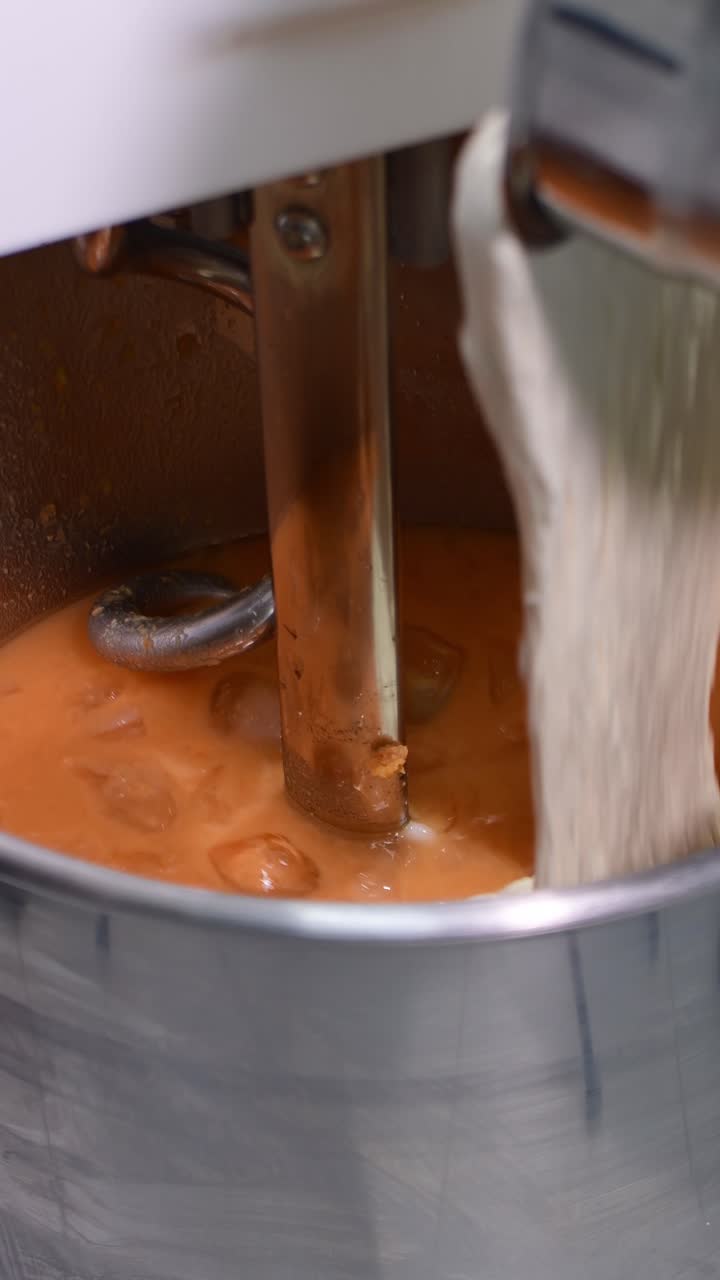 Vertical close-up of sourdough starter being added to a mixture inside an industrial mixer, forming enriched bread dough in a professional bakery environment
