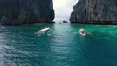 Antenne-Von-Riesigen-Kalksteinfelsen,-Türkisfarbenem-Wasser-Und-Natürlichem-Archipel-Mit-Drohne,-Die-Durch-Felsen-Und-Boote-In-El-Nido,-Palawan,-Philippinen-Fliegt