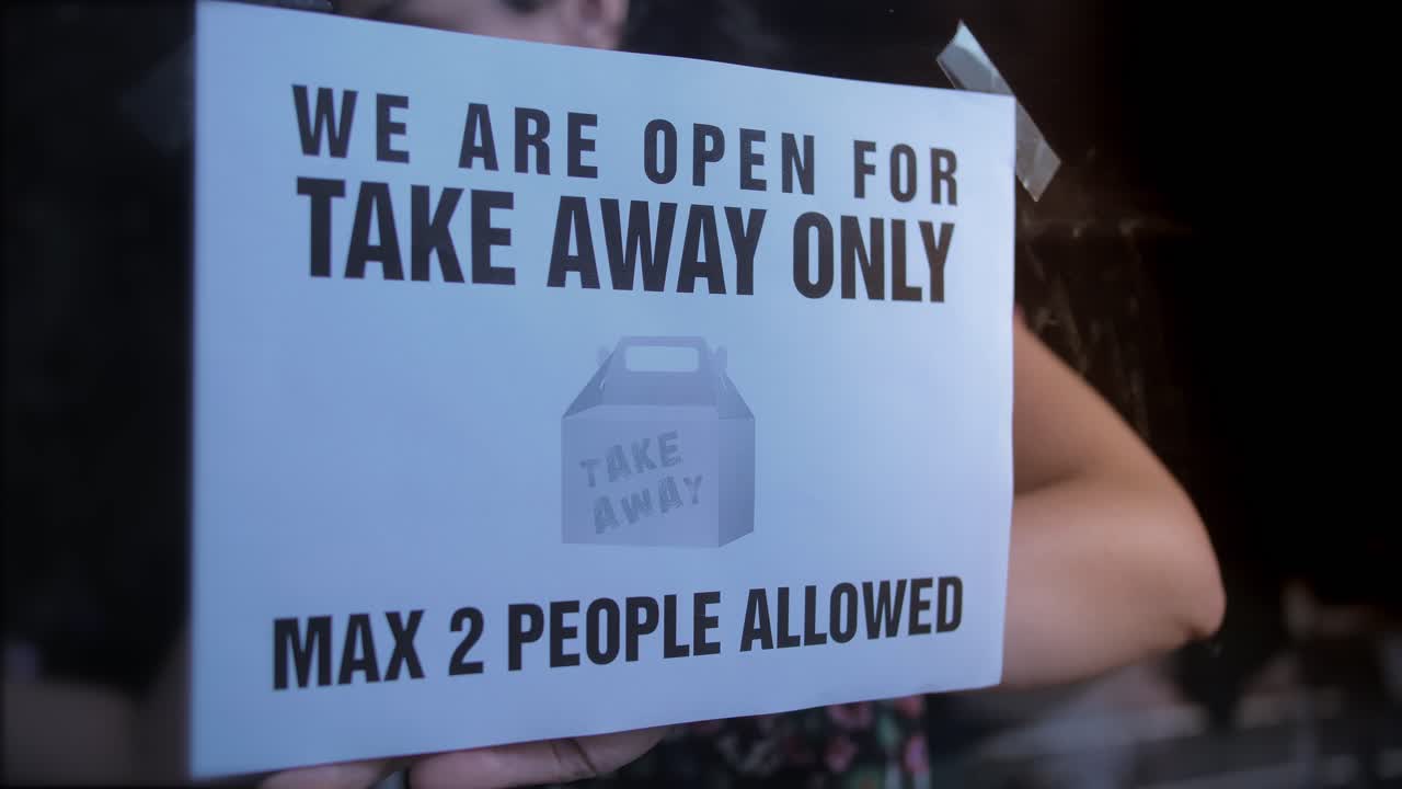 Woman Taping 'Take Away Only' Sign on Shop Window