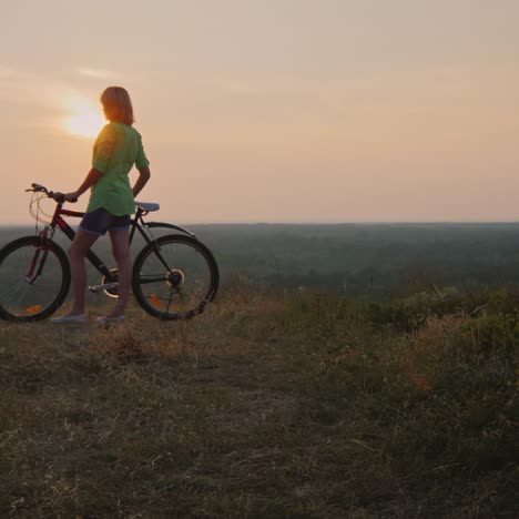 silhouette of a woman with a bicycle admiring the sunset