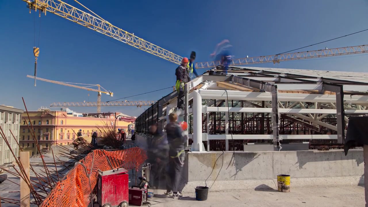 Constructores y carpinteros uniformados trabajando en el tejado, timelapse. Obra de construcción con refuerzo metálico de edificio moderno. Cielo azul nublado de fondo, vista desde la azotea