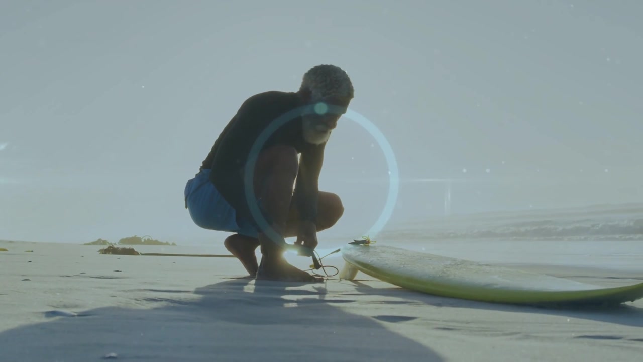 Man fastening surfboard leash while glancing toward ocean, preparing for surfing with HUD on torso
