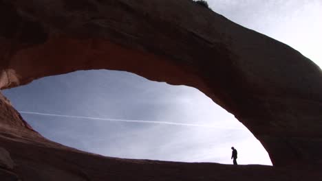 a person walks beneath a giant sandstone arch in arches national park utah