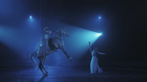 una chica con un vestido blanco levanta un caballo con un jinete bajo una hermosa iluminación, una actuación de circo. cámara lenta