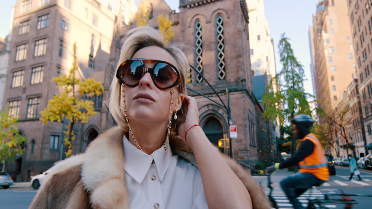 New York, USA, 25 October 2025: Close up portrait of woman wearing oversized designer sunglasses. Medium shot of a blonde woman in a white shirt and fur coat adjusting sunglasses on a city street