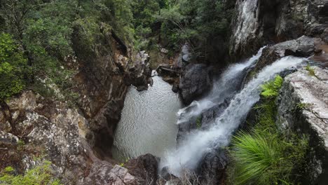 twin waterfalls cascading down an old-growth rainforest into a natural rock formation swimming hole