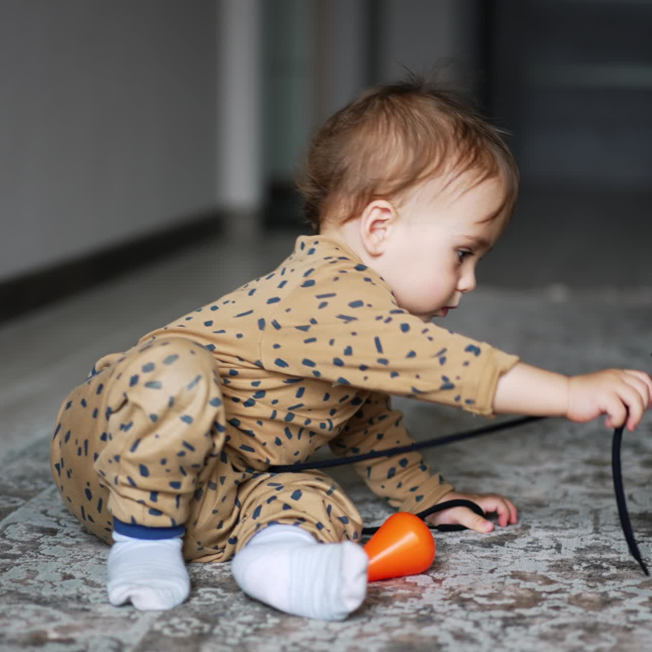 Lovely cute baby boy sitting in the room playing with a shoe lace. Adorable kid throws cord to a black cat sitting beside. Little child playing with cat