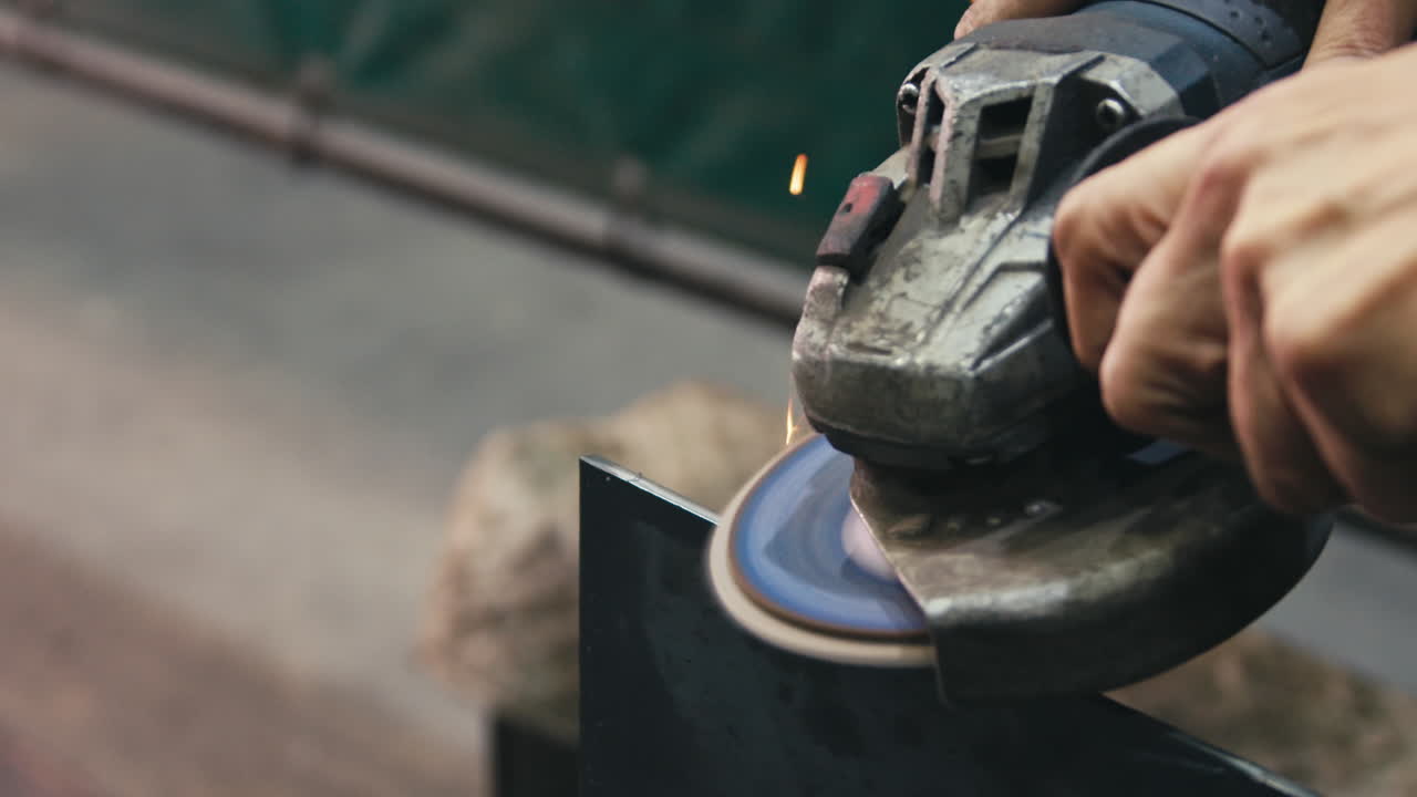 Worker brushing a piece of metal with angle grinder in a workshop. Slow motion.