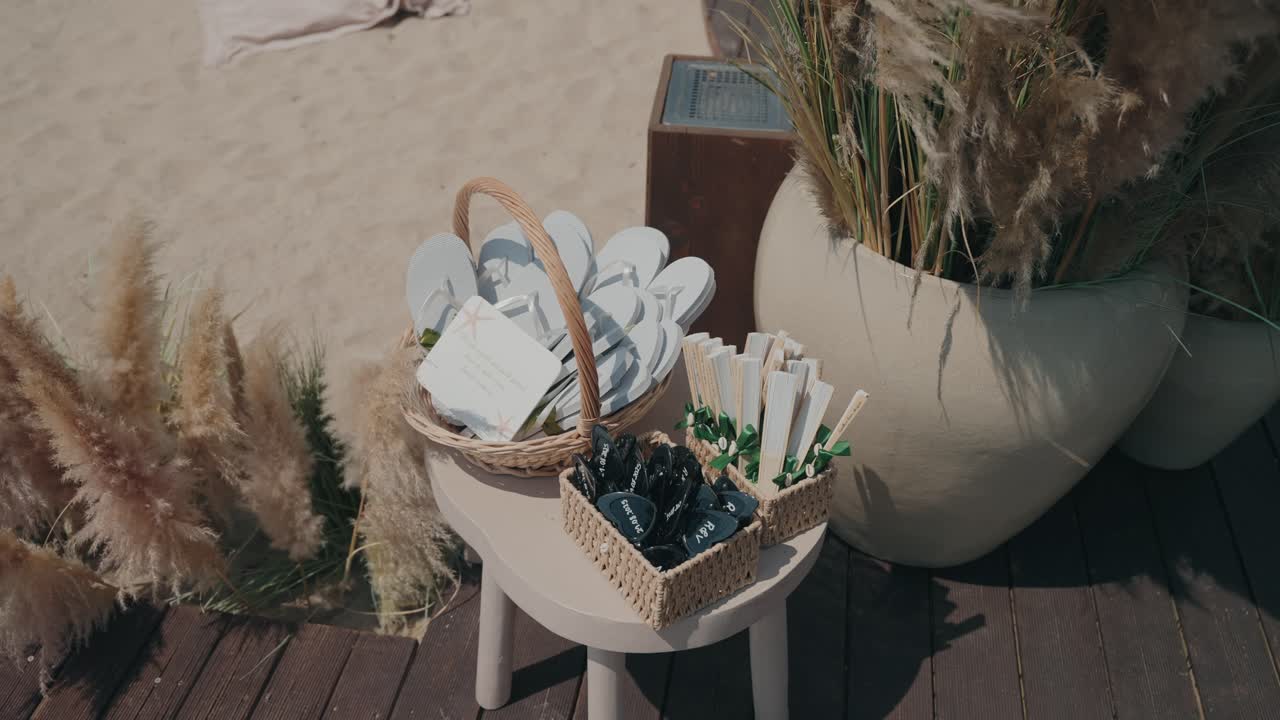 Sunny beach wedding setup with baskets of flip flops, fans, and rustic décor