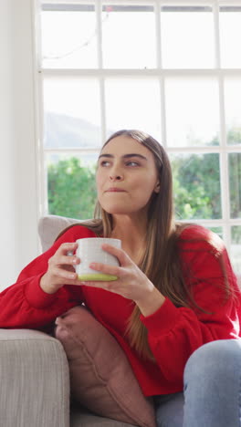 video vertical de una mujer caucásica feliz sentada en el sofá con café