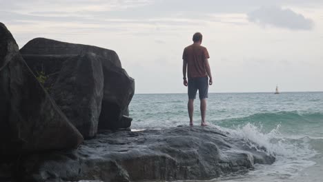 la parte posteriore di un uomo in piedi sulla roccia con le onde che si infrangono a dam trau beach in vietnam