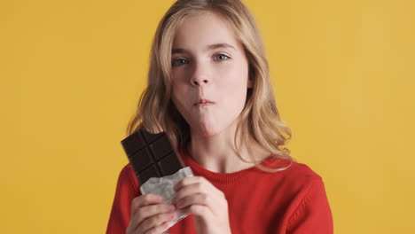 teenage caucasian girl eating chocolate bar in front of the camera.