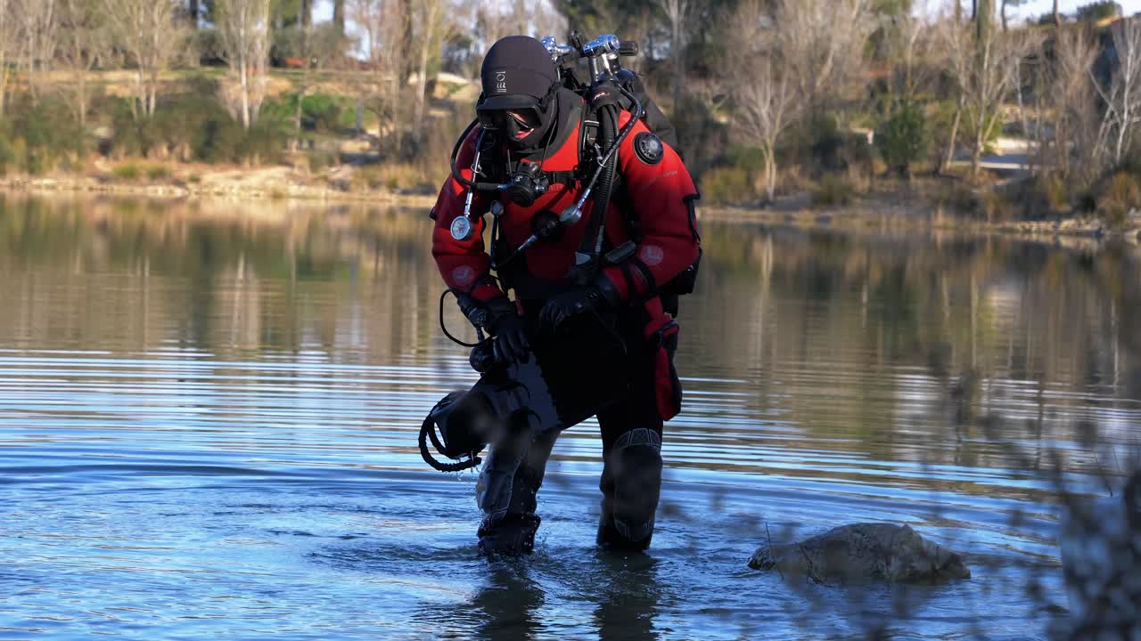A diver grabs his flippers and enters a lake with his red buoy in the middle of winter