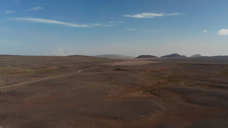 Vista-De-Pájaro-Del-Espectacular-Paisaje-Desértico-En-Islandia.-Vista-Aérea-De-Drones-Del-Panorama-Rocoso-Y-Polvoriento-De-Las-Tierras-Altas-Islandesas-Con-Camino-De-Grava-Y-Montañas-En-Segundo-Plano