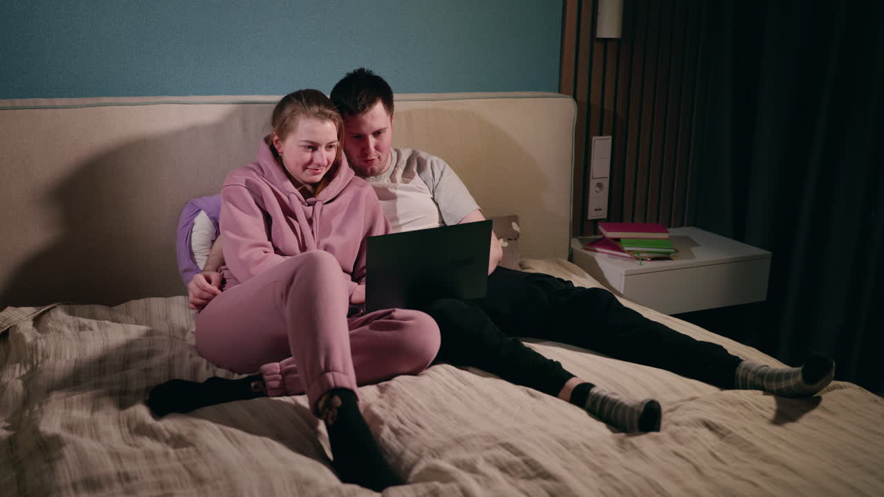 пара отдыхает на кровати с ноутбуком.