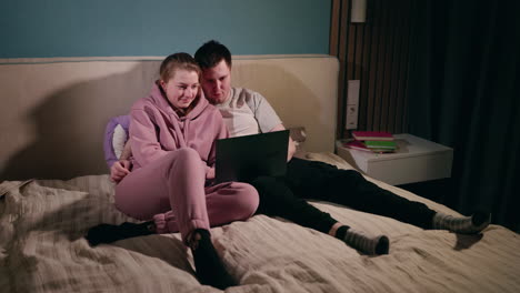 couple relaxing on bed with laptop