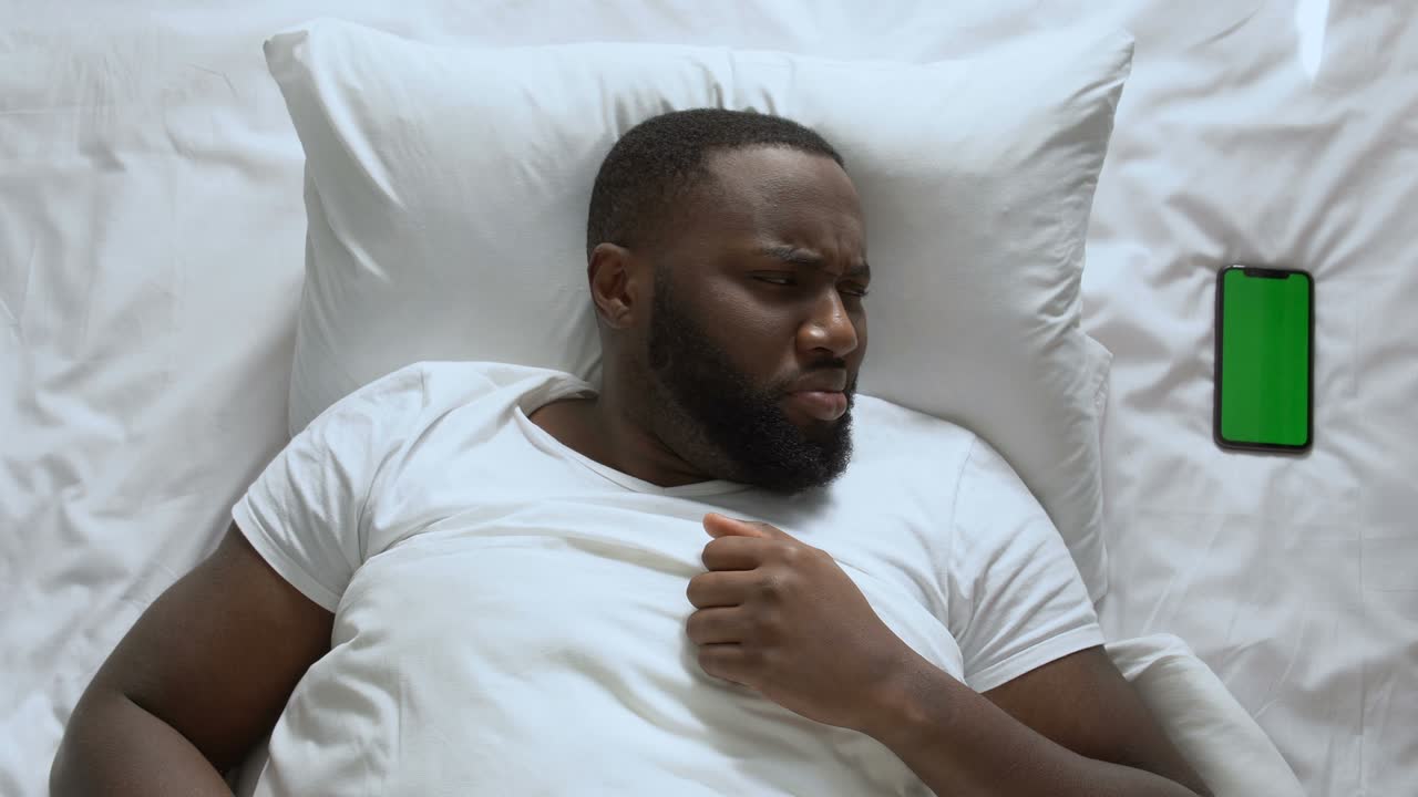 man waking up because of noisy call of his green screen smartphone