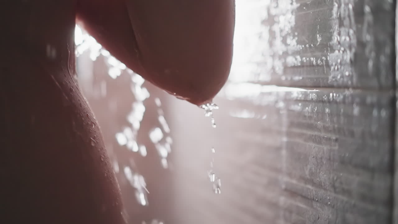 은 여자가 몸 아래로 흐르는 물방울과 함께 샤워를 하고 있습니다. 벌거벗은 여자는 따뜻한 물의 도움으로 몸을 고 샤워합니다. 가운 샤워에서 청소 절차.
