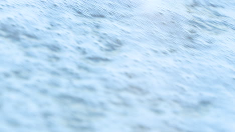 Foamy-sea-waves-crashing-onto-a-sandy-shore,-illustrating-the-relentless-motion-of-the-ocean