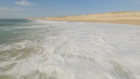 Drone-De-Carreras-Fpv-Aéreo-Volando-Bajo-Sobre-Olas-De-Espuma-A-Lo-Largo-De-La-Costa-De-Una-Playa-Desierta,-Soustons-En-Francia