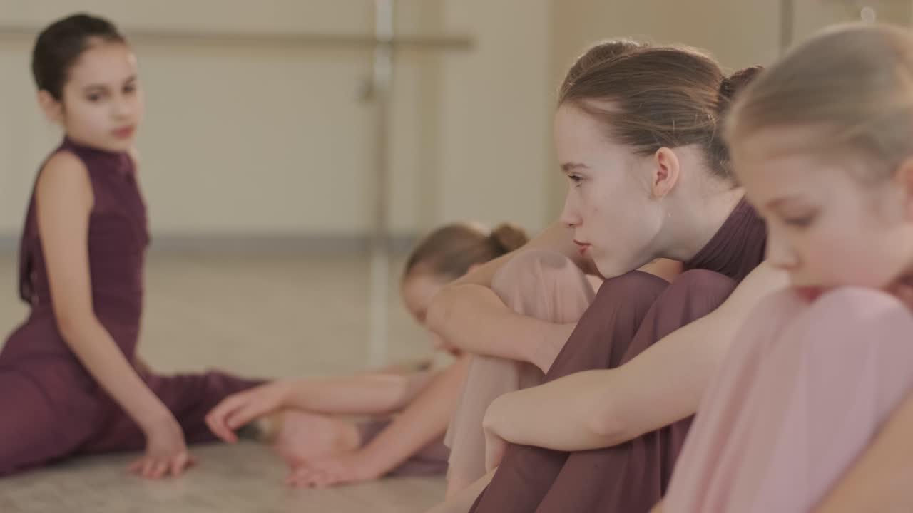 группа молодых студентов балета в черной танцевальной одежде практикует позиции в просторной балетной студии с деревянным полом и настенными решетками. сосредоточенные выражения и синхронизированные движения.