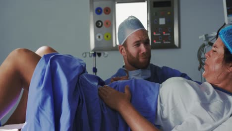 Side-view-of-Caucasian-female-surgeon-examining-pregnant-woman-during-labor-in-operation-theater-at-