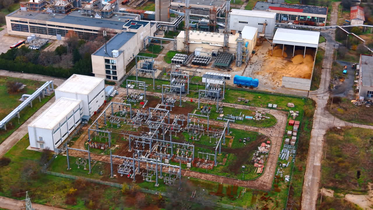 Ovenfra-udsigt over elektrisk transformerstation med transformere og udstyr. Højtliggende optagelse af strømfordelingsanlæg med metalstrukturer, ledninger og industribygninger.