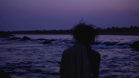 rear view of a monk meditating near the river at twilight, enjoying the purple light of the sunset, creating a peaceful and spiritual atmosphere