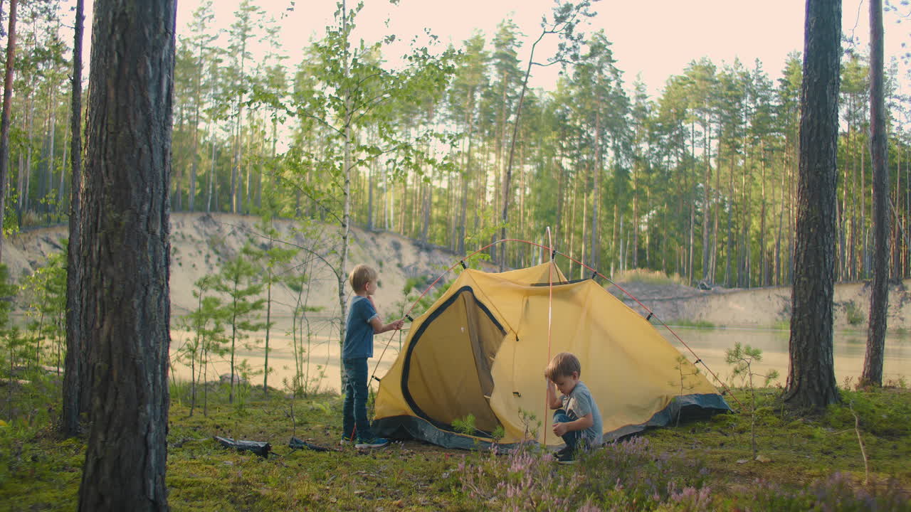 젊은 남자와 두 어린 소년은 함께 캠페인 동안 밤을 보내기 위해 텐트 캠프를 설치했습니다. 아버지와 행복한 어린 시절. 아버지와 아들들은 숲에서 함께 텐트를 설치했습니다.