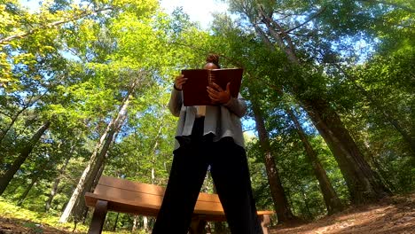 tiro de ángulo bajo de mujer negra de pie en el bosque leyendo la biblia