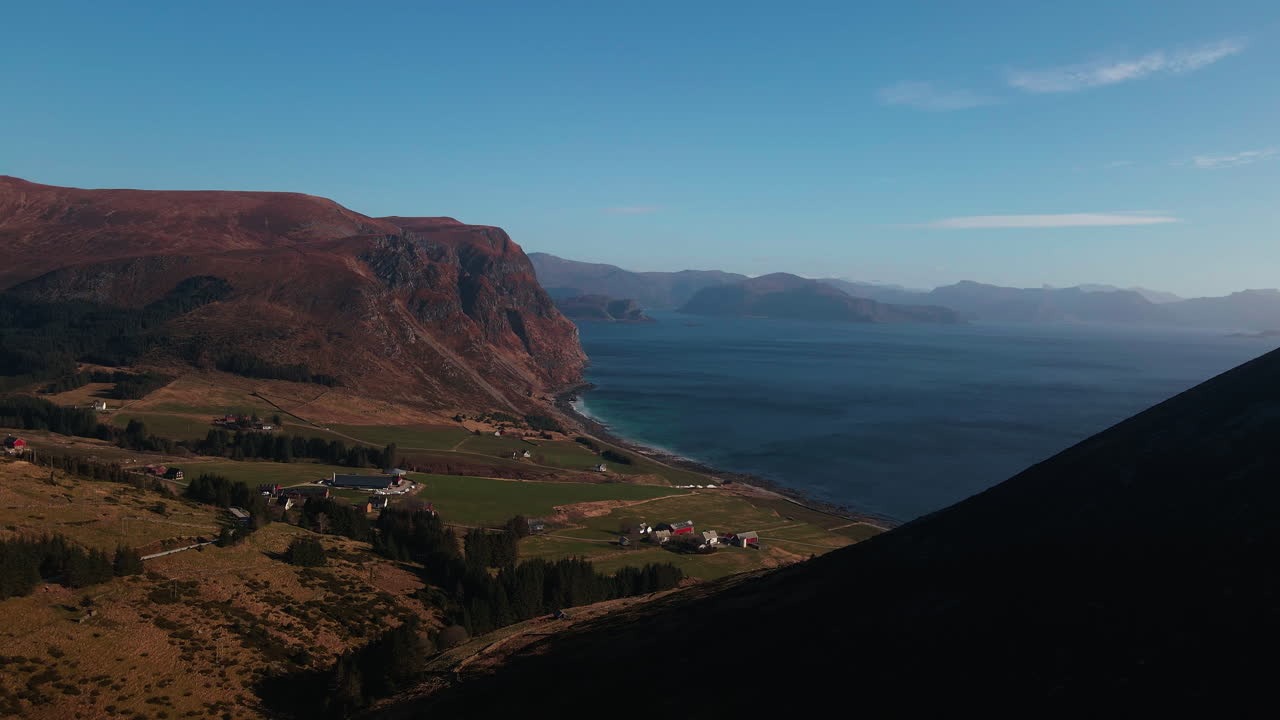 Drone flying over a hill looking towards farms and mountains