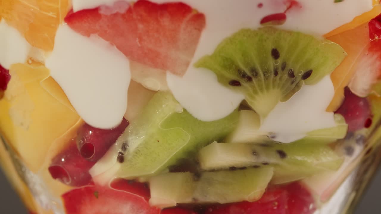 Pouring Yogurt Over Fresh Chopped Fruit in a Glass