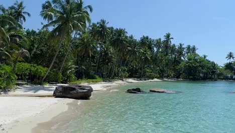 Aerial,-pan-drone-shot-over-the-shallow,-turquoise-sea,-palm-trees-and-a-paradise-beach,-slowly-panning-to-the-left,-on-a-sunny-day,-in-Koh-Kood,-Thailand,-Asia