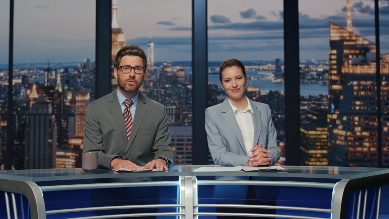 los presentadores transmitiendo noticias de última hora en el estudio. los anfitriones sonrientes hablando.