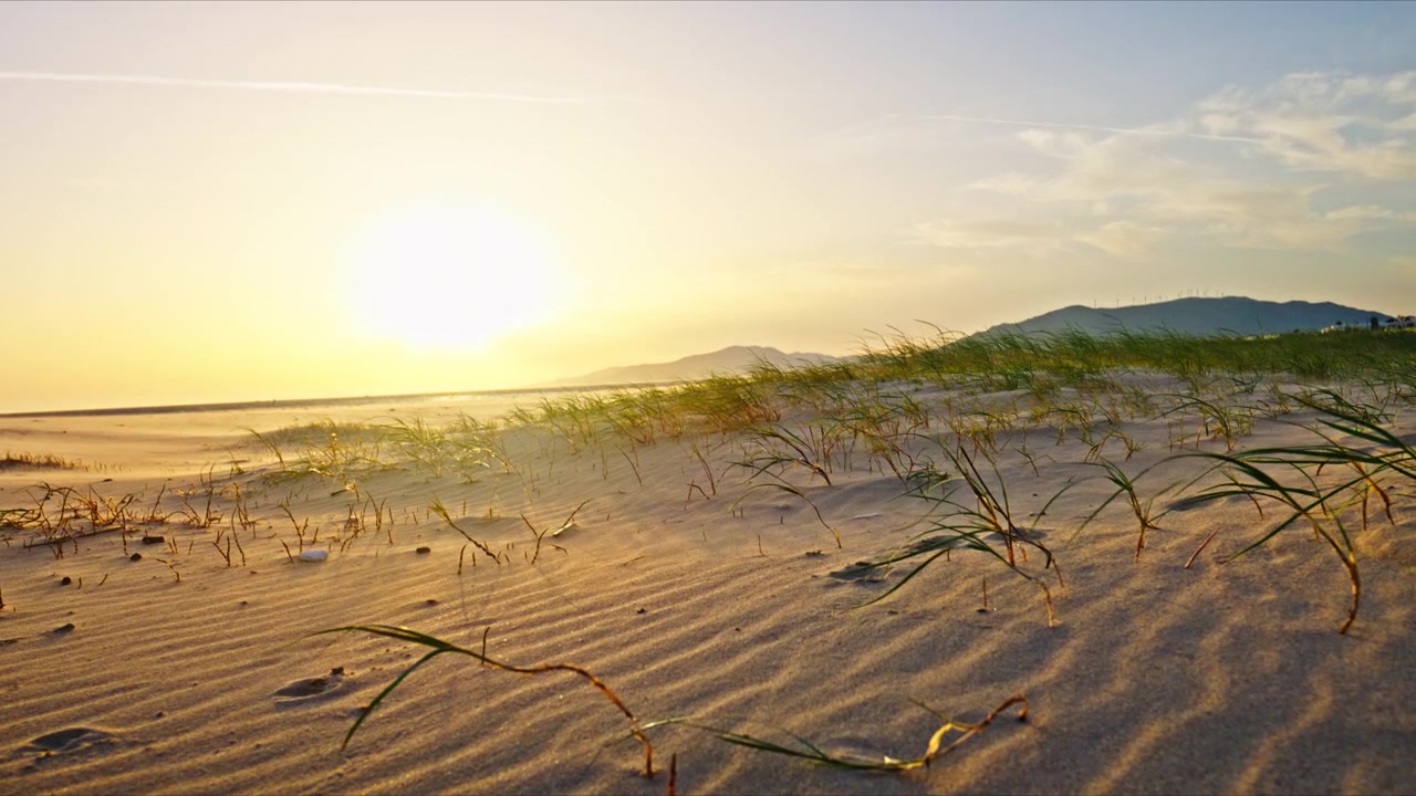 Tramonto dorato sulla spiaggia di Los Lances a Tarifa, Spagna. La calda luce della sera sulle dune di sabbia atlantiche e la costa infinita crea una scena costiera pacifica e cinematografica.