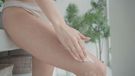 woman applying body lotion to thigh