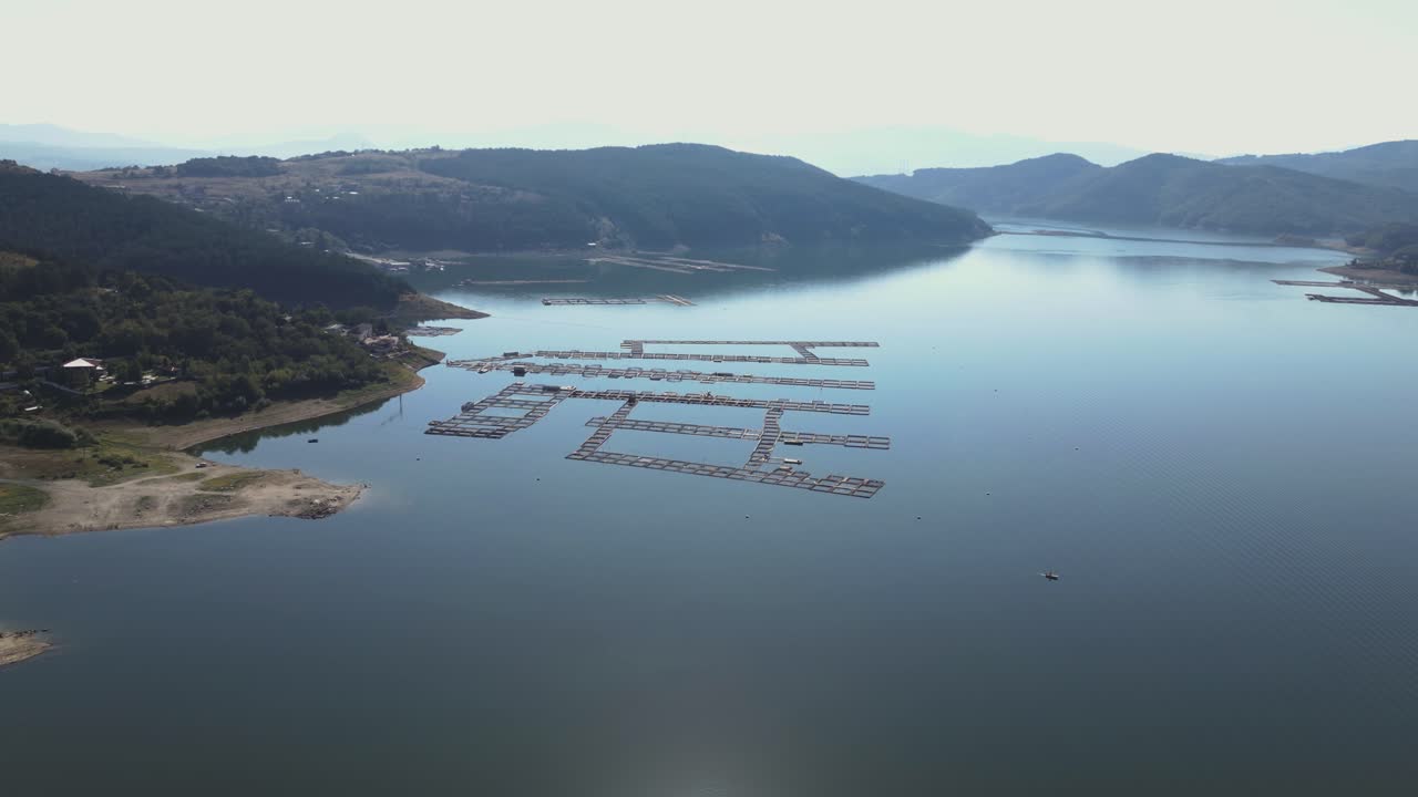 산과 울창한 풍경으로 둘러싸인 저수지의 조용한 물 위에 떠다니는 조직된 물고기 농장의 공중 촬영