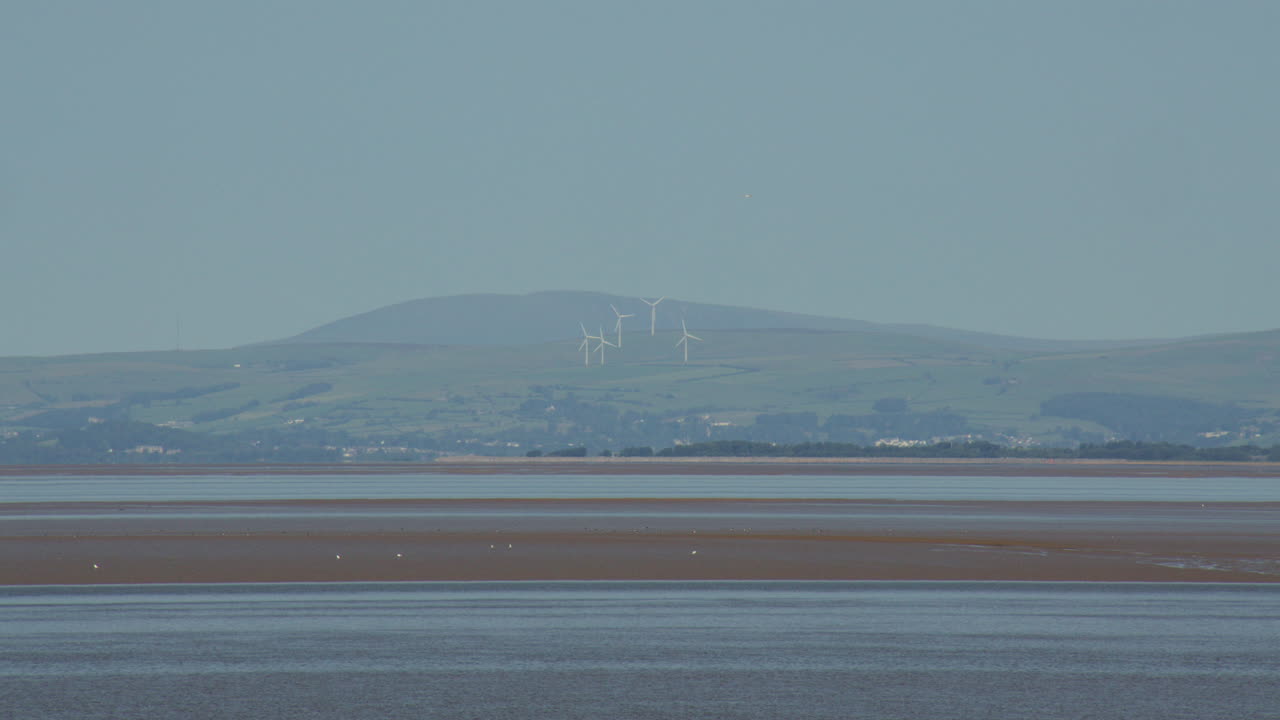 Extra wide shot of the Kent Estuary at low tide with Grange over Sands and the Lakeland Fells at Bolton le Sands, The shore car park. Wind turbines in background