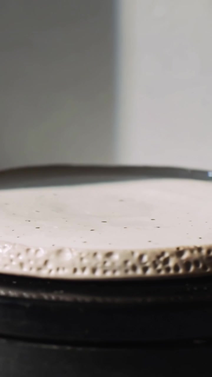 Vertical video: Rising camera showing ceramic disc tilting on stack base in studio, exposing rim