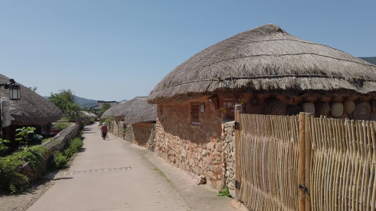 un trabajador de mantenimiento de la aldea con un palo de escoba caminando por un camino entre casas con techo de paja en la aldea popular de nagan eupseong cerca de la bahía de suncheon, corea del sur