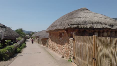 a village maintenance worker with a broomstick walking on a path between thatched roof houses in nagan eupseong folk village near suncheon bay, south korea