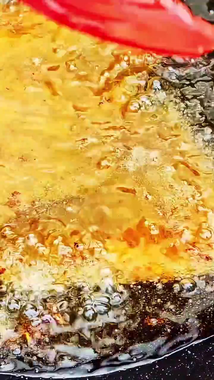 Vertical close-up of a battered item sizzling in golden boiling oil in a deep frying pan