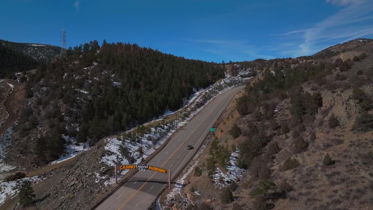 Winter Central City Parkway highway road bridge Idaho Springs Blackhawk Colorado aerial drone welcome sign snow blue sky sunny clouds forest power lines Clear Creek Gilpin County backwards motion