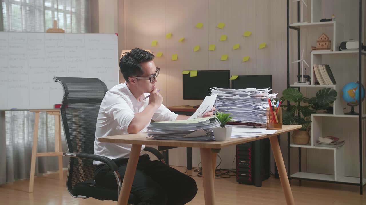 Asian Man Thinking And Looking At Paper Then Raising Index Finger While Working With Documents At The Office