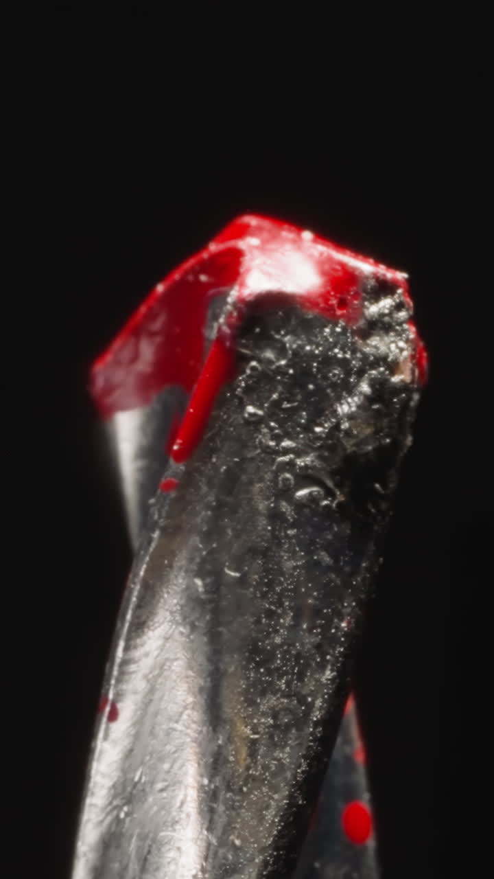 Twisted pobedite alloy tip of masonry drill bit in red paint at bright studio light. Professional tool used for making holes on black background macro