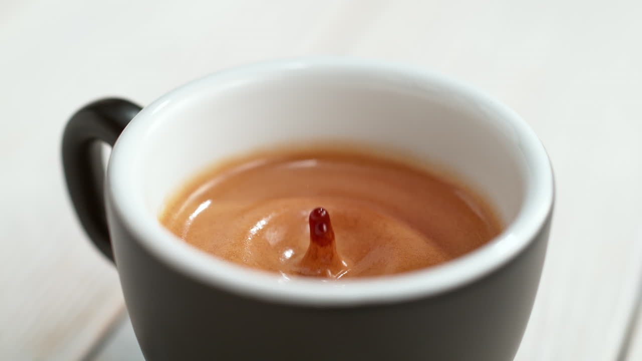 에스프레소 방울이 커피 컵에 떨어지고 부드러운 크레마가 매크로와 느린 동작, 밝은 배경으로 스프레이를 만니다.