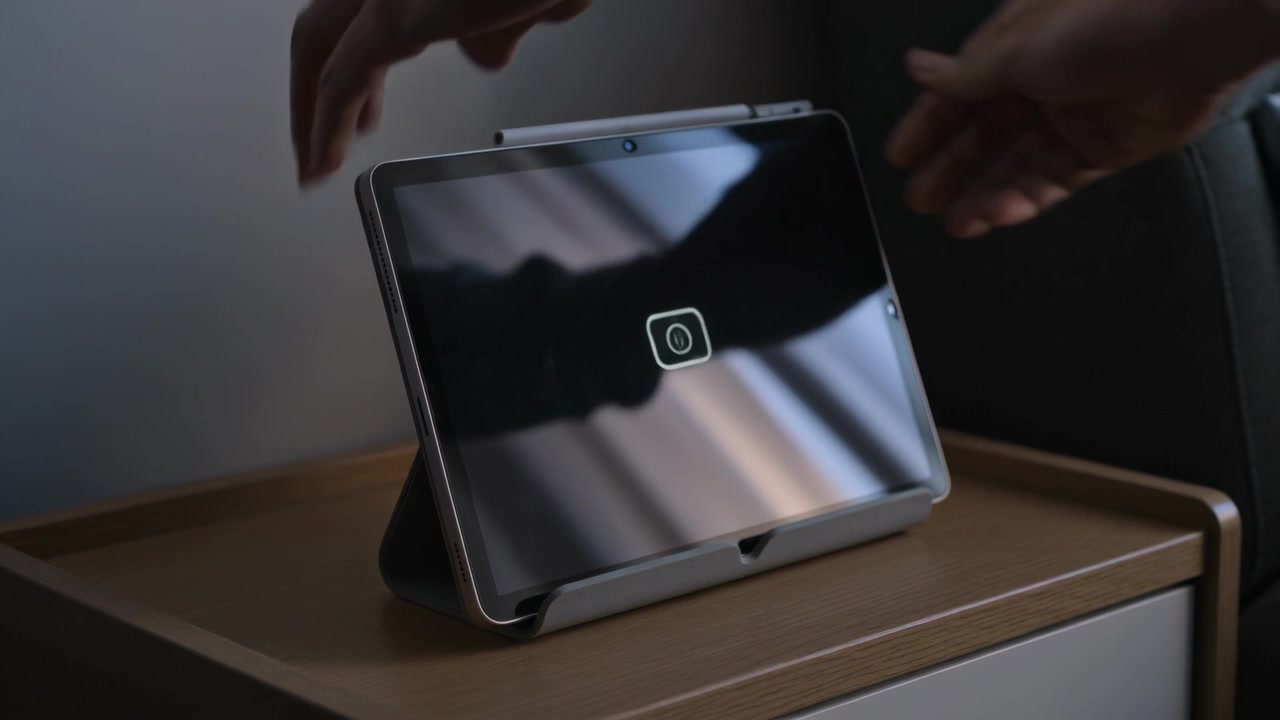 Holding tablet, hands lowering it into folded folio stand on nightstand, snapping cover for use