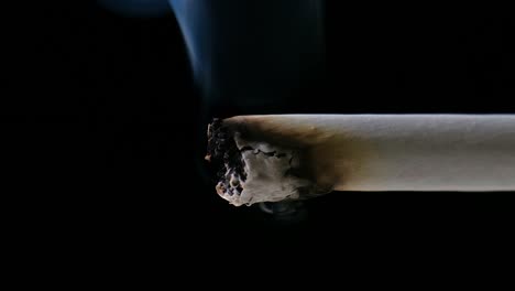 tip of a cigarette slowly consuming itself, emitting a trail of smoke, in front of a black background